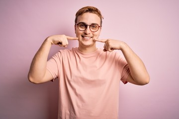 Young handsome redhead man wearing casual t-shirt standing over isolated pink background smiling cheerful showing and pointing with fingers teeth and mouth. Dental health concept.
