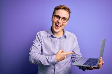 Young handsome redhead businessman working using laptop over purple background very happy pointing with hand and finger