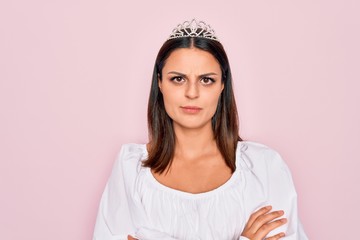 Young beautiful brunette woman wearing princess tiara standing over isolated pink background skeptic and nervous, disapproving expression on face with crossed arms. Negative person. © Krakenimages.com