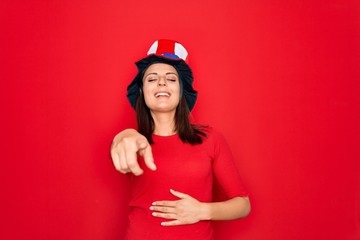 Young beautiful brunette woman wearing united states hat celebrating independence day laughing at you, pointing finger to the camera with hand over body, shame expression