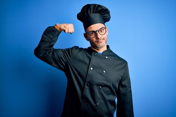 Young handsome chef man wearing cooker uniform and hat over isolated blue background Strong person showing arm muscle, confident and proud of power