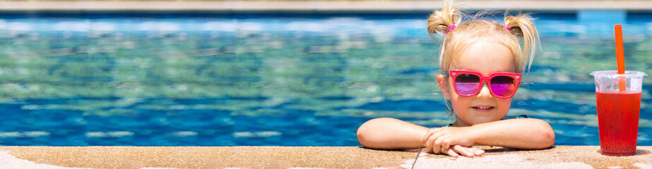 Beautiful little girl, cute toddler with blonde hair in swimwear, sitting at a swimming pool and...