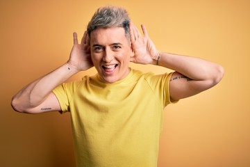 Young handsome modern man wearing yellow shirt over yellow isolated background Smiling cheerful playing peek a boo with hands showing face. Surprised and exited