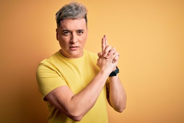 Young handsome modern man wearing yellow shirt over yellow isolated background Holding symbolic gun with hand gesture, playing killing shooting weapons, angry face