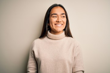 Fototapeta premium Young beautiful asian woman wearing casual turtleneck sweater over white background looking away to side with smile on face, natural expression. Laughing confident.