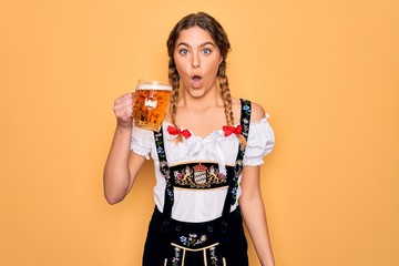 Beautiful blonde german woman with blue eyes wearing octoberfest dress drinking jar of beer scared in shock with a surprise face, afraid and excited with fear expression