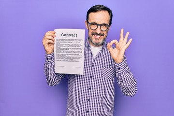 Middle age handsome man wearing glasses holding contract document over purple background doing ok sign with fingers, smiling friendly gesturing excellent symbol