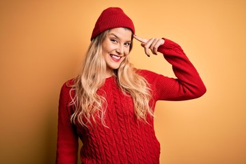 Young beautiful blonde woman wearing casual sweater and wool cap over white background Smiling pointing to head with one finger, great idea or thought, good memory