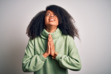 Young beautiful african american woman with afro hair wearing green winter sweater begging and...