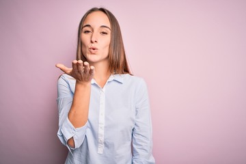 Young beautiful businesswoman wearing elegant shirt standing over isolated pink background looking at the camera blowing a kiss with hand on air being lovely and sexy. Love expression.