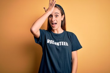 Young beautiful woman wearing volunteer t-shirt doing volunteering over yellow background surprised...