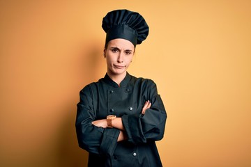 Young beautiful chef woman wearing cooker uniform and hat standing over yellow background skeptic and nervous, disapproving expression on face with crossed arms. Negative person.