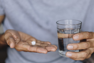 Sick man with a glass of water and pills, Taking medication to alleviate illness