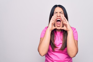 Young beautiful brunette woman wearing casual pink t-shirt standing over white background Shouting...