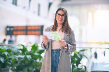 Young beautiful woman smiling happy and confident. Standing with smile on face  holding tickets at train station