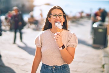 Young beautiful woman on vacation smiling happy and confident. Standing with smile on face eating ice cream walking at the city