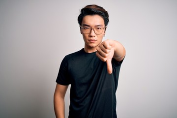 Young handsome chinese man wearing black t-shirt and glasses over white background looking unhappy and angry showing rejection and negative with thumbs down gesture. Bad expression.