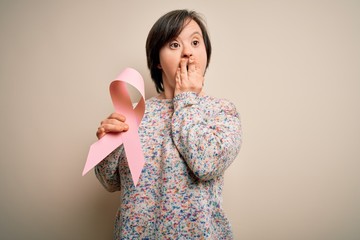 Young down syndrome woman holding breast cancer awareness pink ribbon cover mouth with hand shocked...