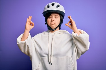 Young down syndrome cyclist woman wearing security bike helmet over purple background relax and smiling with eyes closed doing meditation gesture with fingers. Yoga concept.