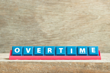 Tile letter on red rack in word overtime on wood background