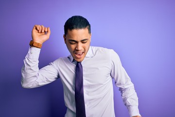 Young brazilian businessman wearing elegant tie standing over isolated purple background Dancing happy and cheerful, smiling moving casual and confident listening to music