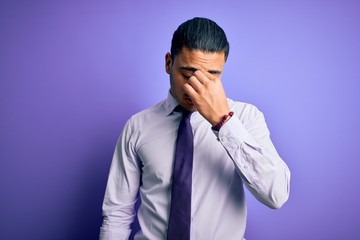 Obraz premium Young brazilian businessman wearing elegant tie standing over isolated purple background tired rubbing nose and eyes feeling fatigue and headache. Stress and frustration concept.
