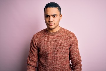 Young brazilian man wearing casual sweater standing over isolated pink background skeptic and...