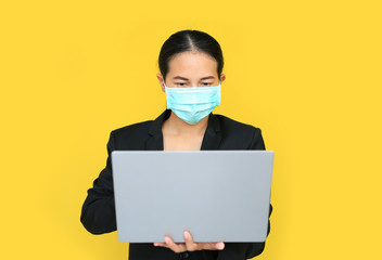 Asian business woman wearing medical shielding mask working with laptop computer isolated on yellow background.