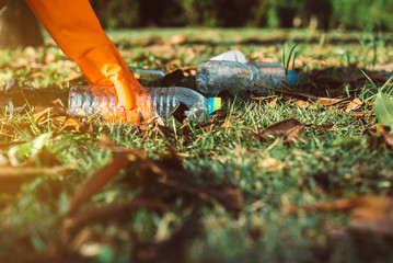 Volunteer woman hands wearing glove and keep plastic bottle from grass floor at public park,Dispose recycle and waste management concept,Environmentally friendly