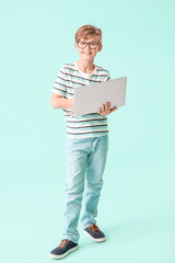 Cute little boy with laptop on color background. Concept of online education