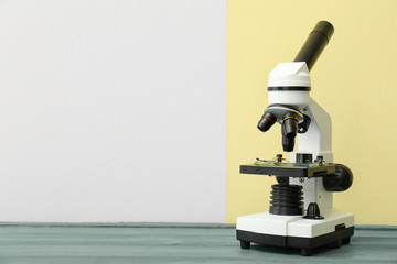 Modern microscope on table against color background