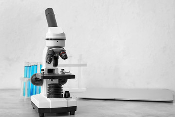 Modern microscope, test tubes and laptop on table