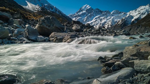 Time lapse of glacier wate cascading down a rocky river with snow-covered mountain peaks and the Hooker valley glacier in the background. Motion time lapse photography captured at Mt Cook, New Zealand