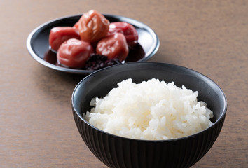 Japanese pickled plums and freshly cooked rice set against a wooden backdrop