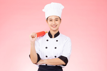 Beautiful Asian chef woman smile and holding rolling pin isolated on pink background,Happiness and Cheerful Professional chef Concept