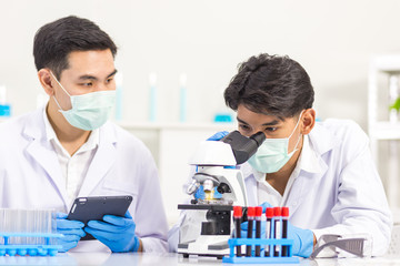 Health care researchers working in biological science laboratories, a researcher uses a microscopic and his assistant using a tablet computer to analyze information of the virus in the laboratory