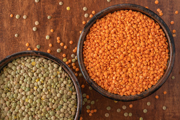 Red lentils and green lentils close up in a bowls on wooden background, view from above
