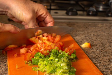 Woman hand cutting red raw tomatoes over orange cutting board