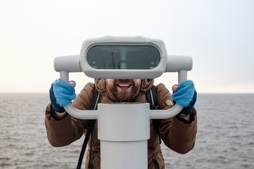 Joyful, smiling man looks with interest at the tower viewer, standing on the promenade, against the...