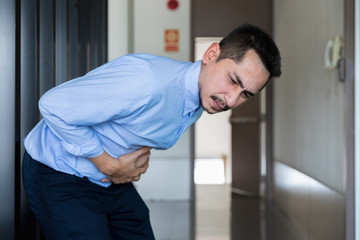 Young businessman stomach ache while in workplace.