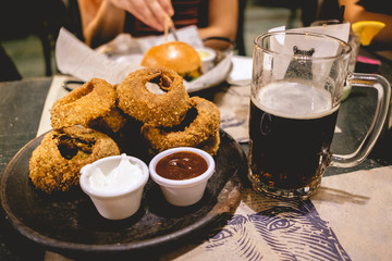Dark craft beer shop and fried onion rings with mayo and barbecue sauce over a paper tablecloth...