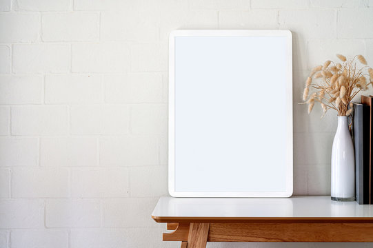 Mockup blank wooden picture frame on white top table with white brick wall in contemporary room.
