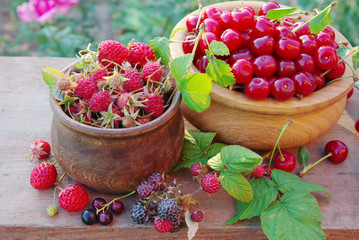 Two wooden bowls with raspberries and cherries. Natural background