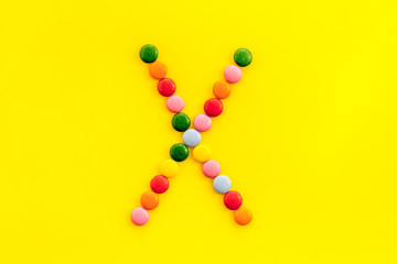 Letter X - alphabet made with sweets on yellow from above