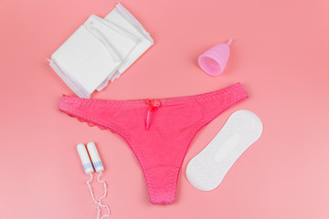 Women's panties with menstrual cups, sanitary pads and tampons on pastel pink background. Top view. Concept of critical days, menstruation, feminine hygiene