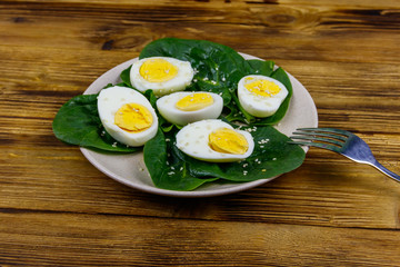 Boiled eggs with fresh spinach leaves and sesame seeds on wooden table