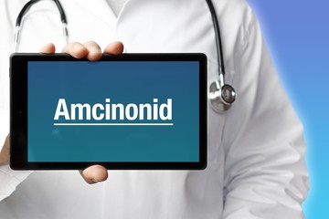 Amcinonid. Arzt mit Stethoskop hält Tablet-Computer in Hand. Text im Display. Blauer Hintergrund. Krankheit, Gesundheit, Medizin