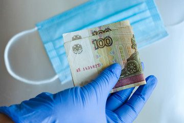 Hands in gloves holding the bill for a hundred rubles on the background of medical masks. Concept of the shortage and increase in the cost of personal protective equipment during the pandemic.