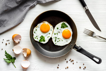 Fried eggs on frying pan on white table top-down
