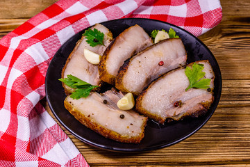 Slices of baked pork belly, garlic and parsley on a black plate